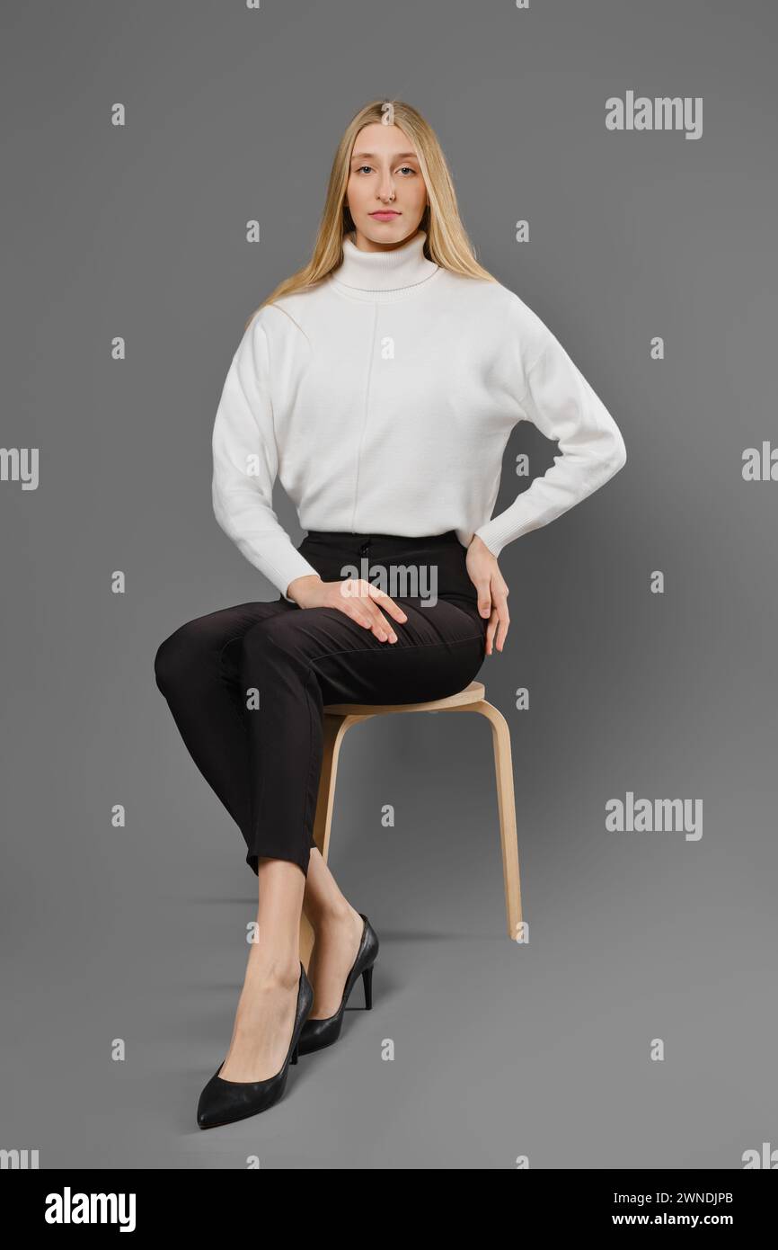 Long-legged young woman woman in tight trousers and sweater sitting on a chair in a beautiful pose Stock Photo