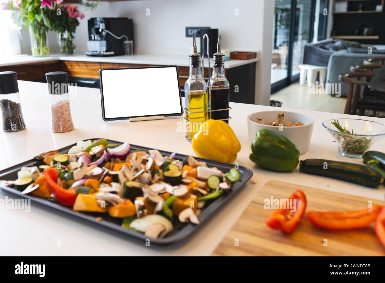 A variety of chopped vegetables are ready on a tray, with a tablet and cooking oils nearby Stock Photo