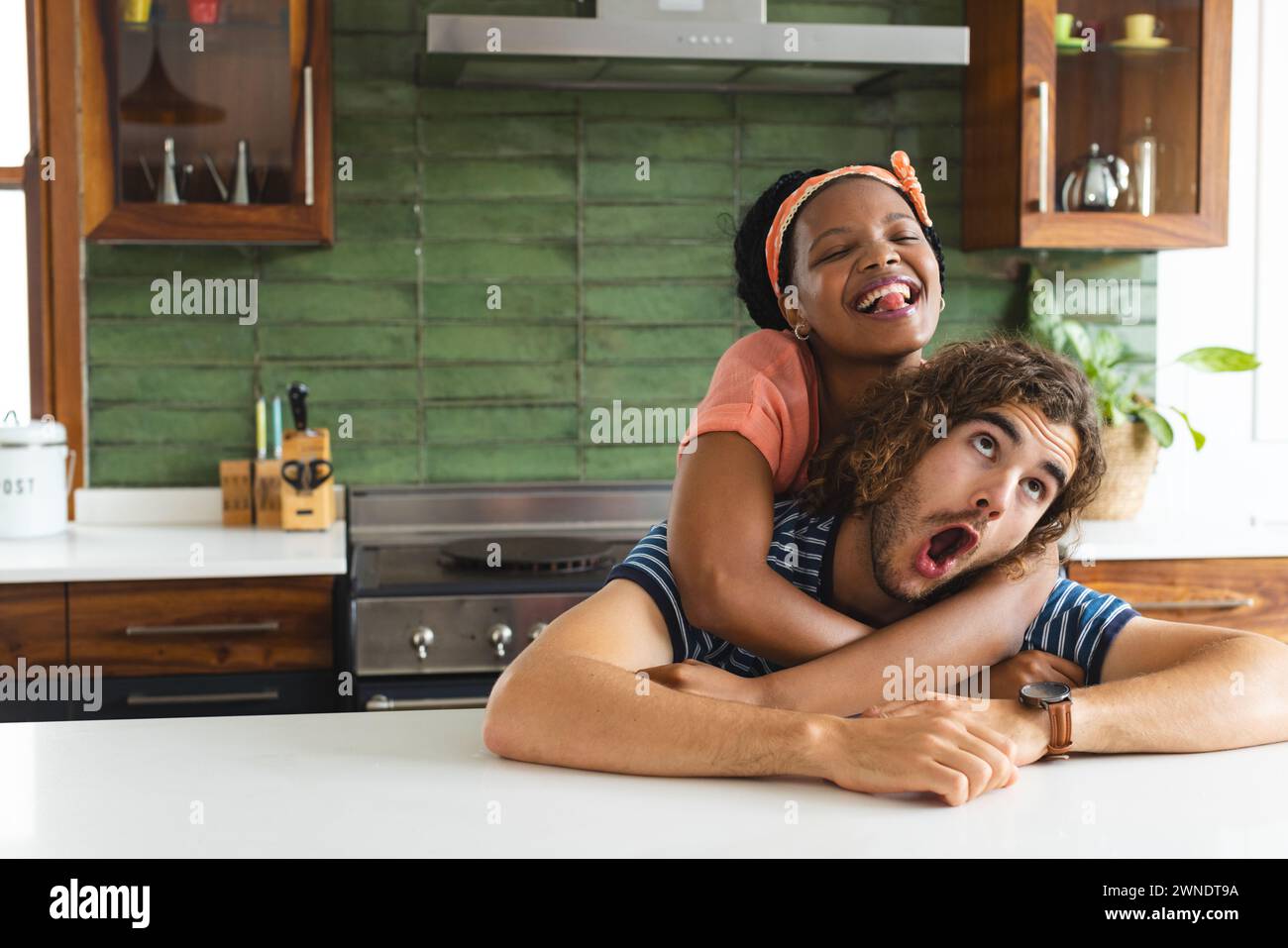 Joyful diverse couple shares a laugh in a bright kitchen. Stock Photo