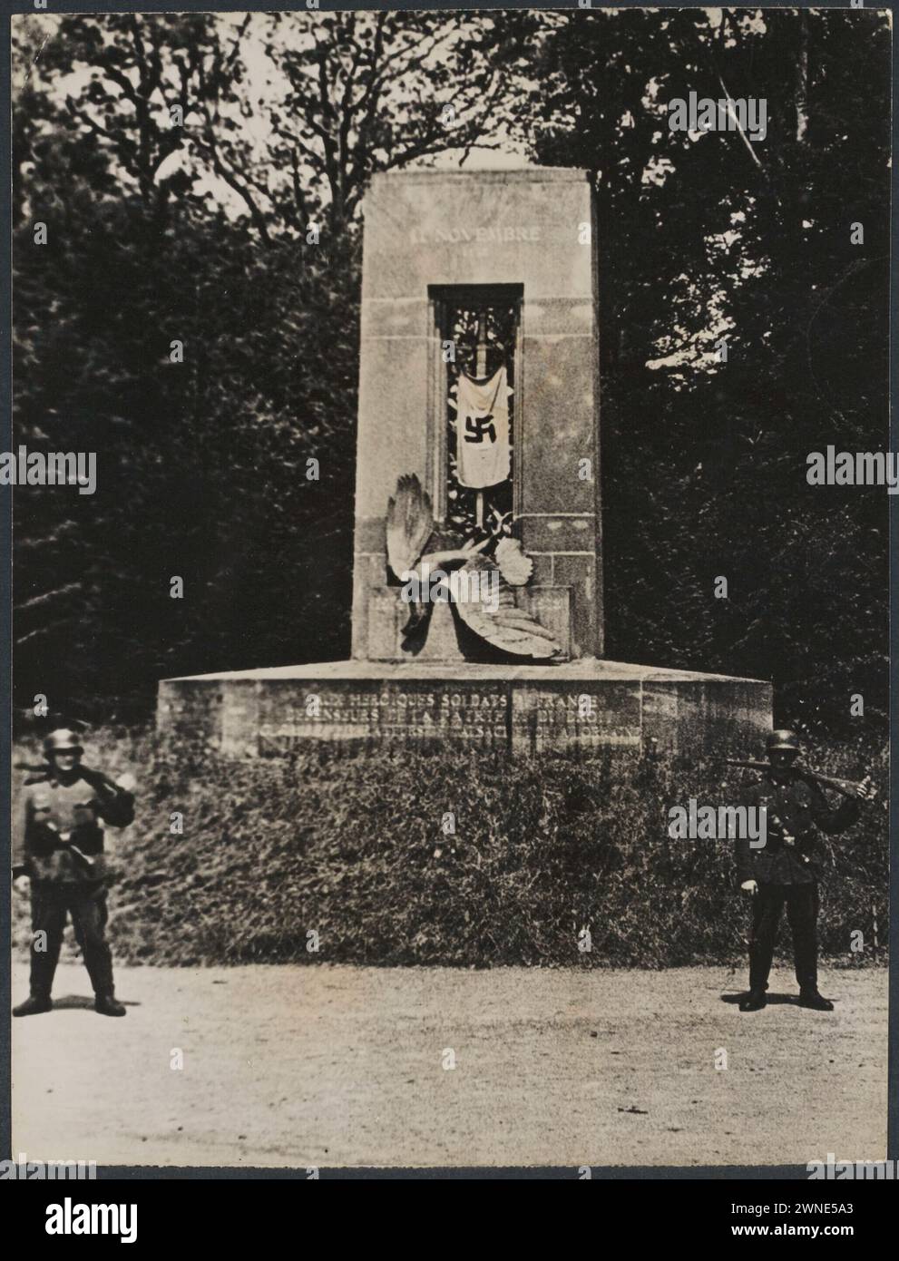 German Nazi flag hangs from a memorial in the Compiègne Forest (france). Two German soldiers before that   June 21, 1940 Stock Photo
