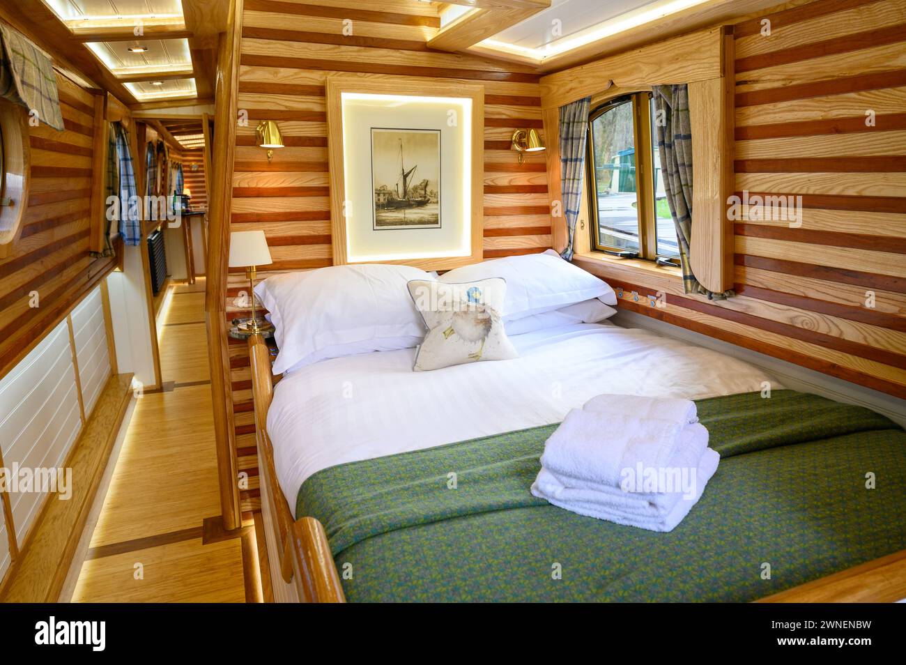 Comforable looking double bed in a hire boat on the inland waterways in Wales with bedding and a pile of towels on the bed. Stock Photo