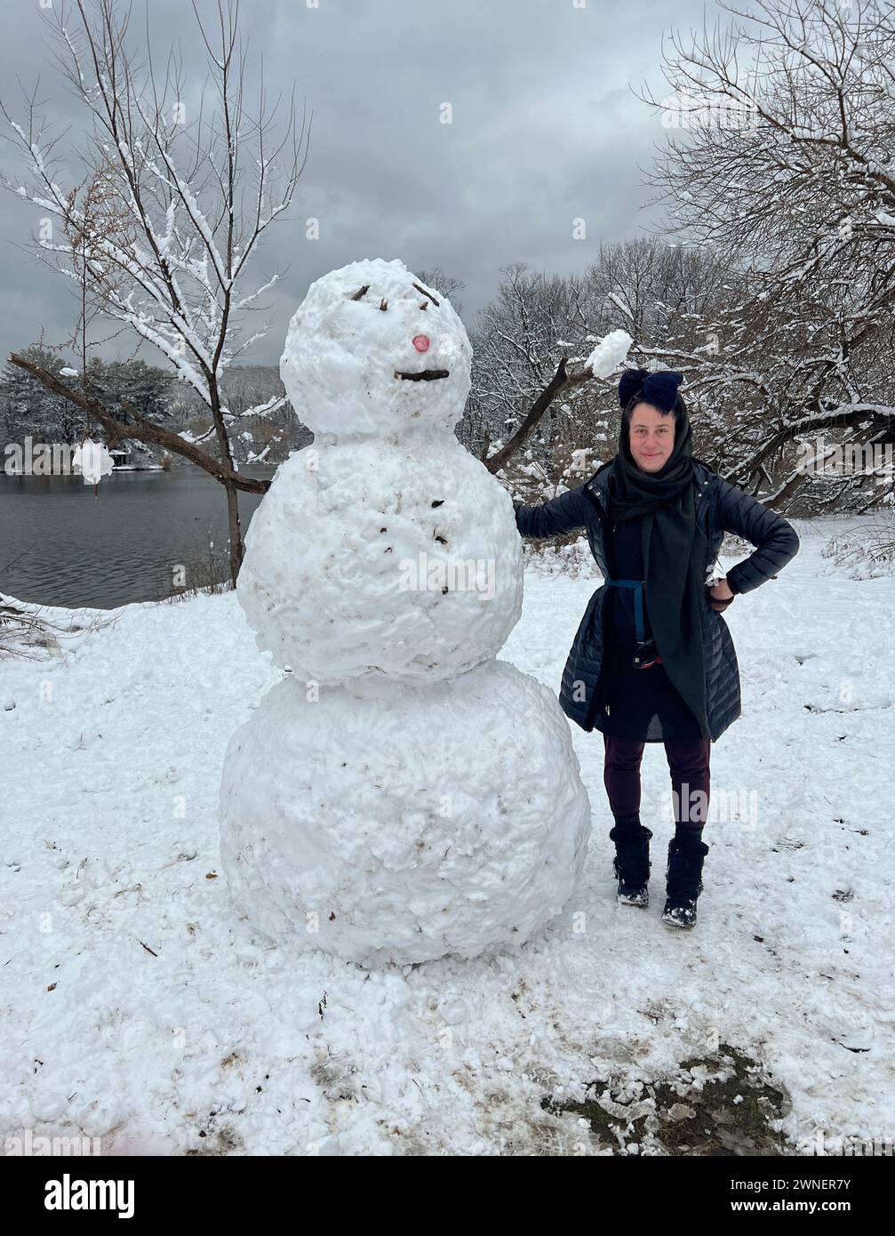 Woman standing next to her snowman in Prospect Park, Brooklyn, New York. Stock Photo
