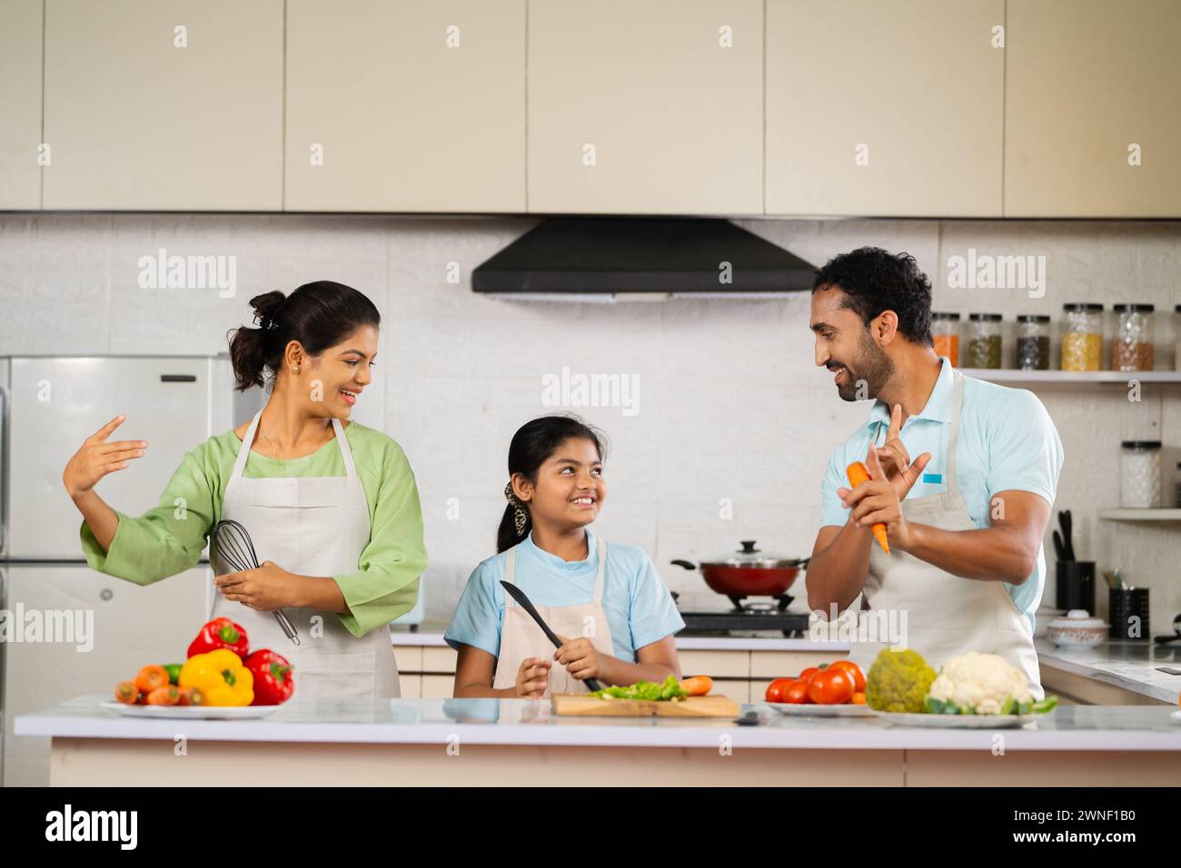 Joyful Indian father mother and kid dancing together at kitchen while cooking during weekend holidays - concept of family bonding, entertainment and Stock Photo