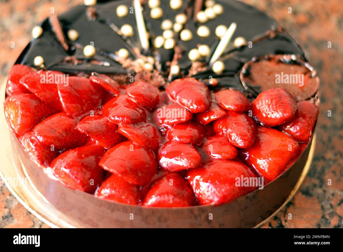 A decorated half and half birthday cake of a sponge cake with whipped cream and chocolate paste topped with chocolate pieces and fresh strawberry frui Stock Photo