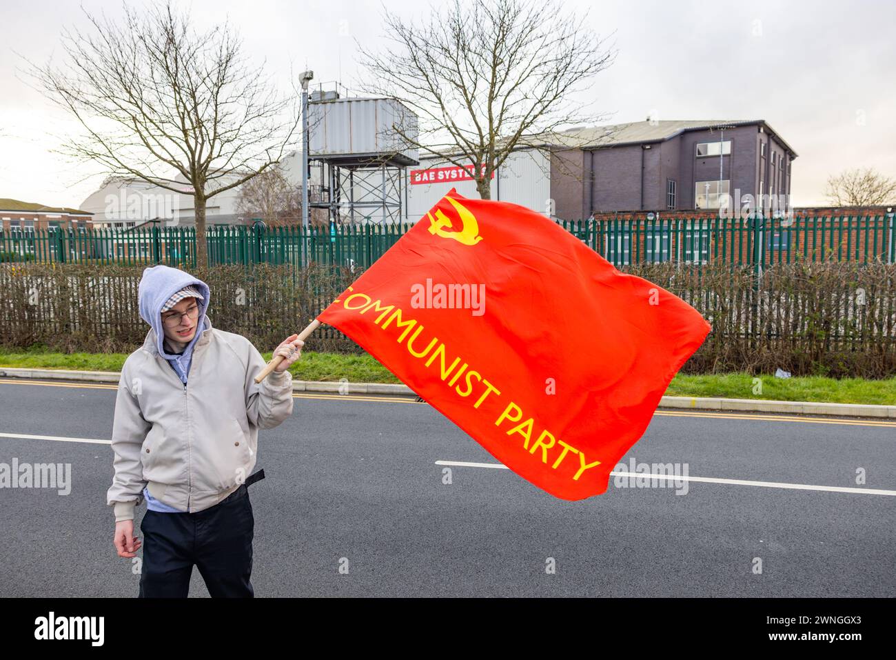 Brough, UK. 02 MAR, 2024. Demonstrator holds a Communist Party of Great Britain flag on the road outside the BAE factory in Brough. Story: A protest organised by members of the Young Communist League outside the BAE systems factory in Brough, 12 miles West of Hull. The factory was used in the development of the F-35 aircraft used by Israeli government. Around 33 protestors no arrests. Credit Milo Chandler/Alamy Live News Stock Photo