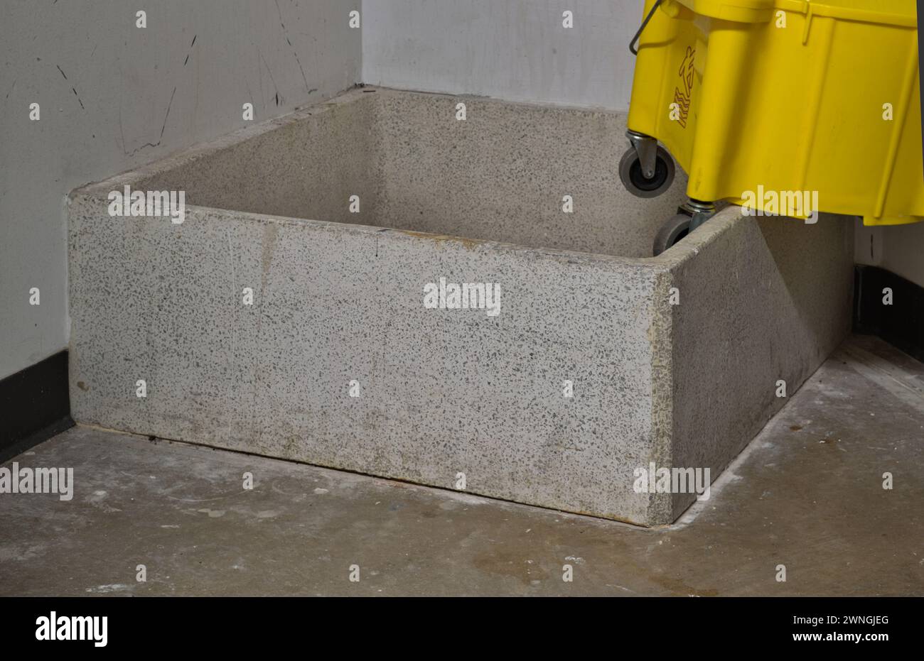 Janitor closet drain and wash basin with a partial mop bucket sitting on top. Janitorial supplies and custodian occupation. Stock Photo
