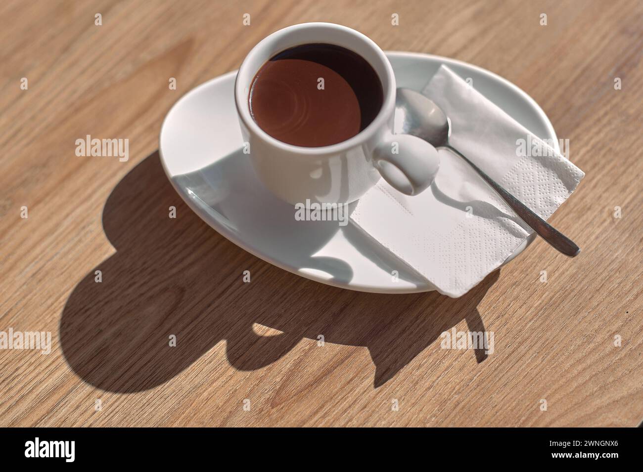 Cup of chocolate on a wooden table, illuminated by sunlight creating an artistic shadow. Stock Photo