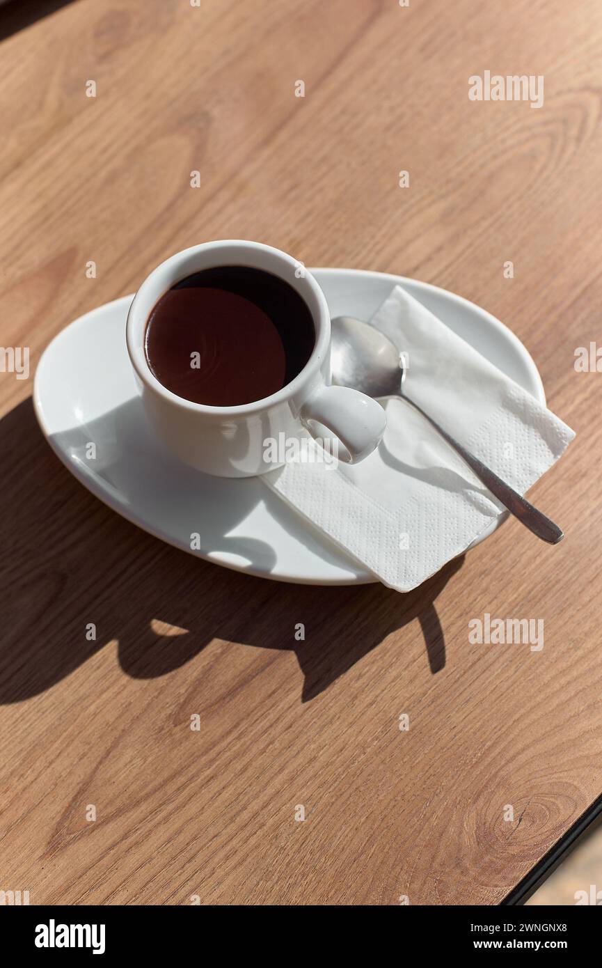 Cup of chocolate on a wooden table, illuminated by sunlight creating an artistic shadow. Stock Photo