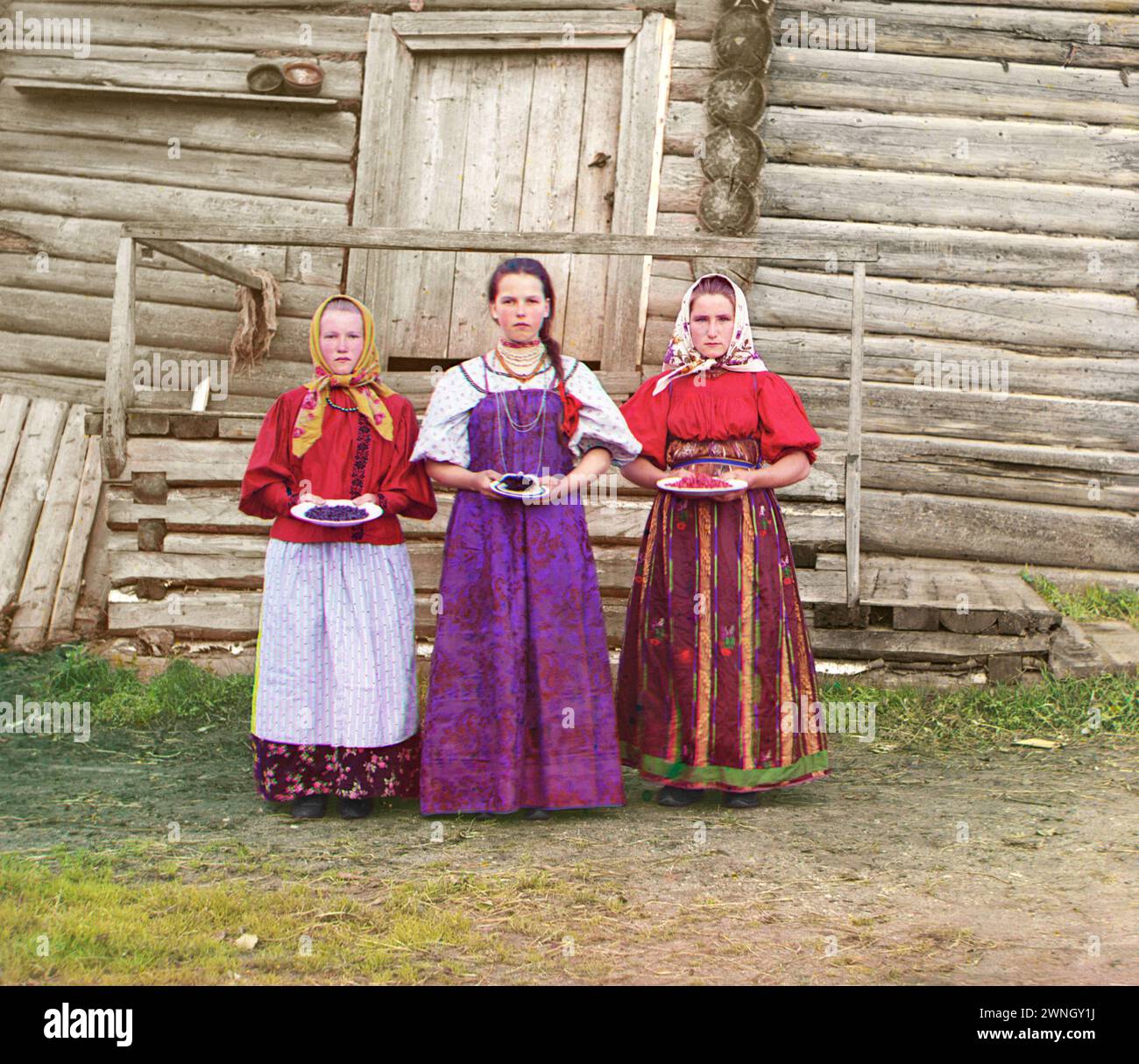 Young Russian peasant women in front of traditional wooden house, in a rural area along the Sheksna River near the small town of Kirillov. Early color photograph from Russia, created by Sergei Mikhailovich Prokudin-Gorskii as part of his work to document the Russian Empire.  1909 Stock Photo
