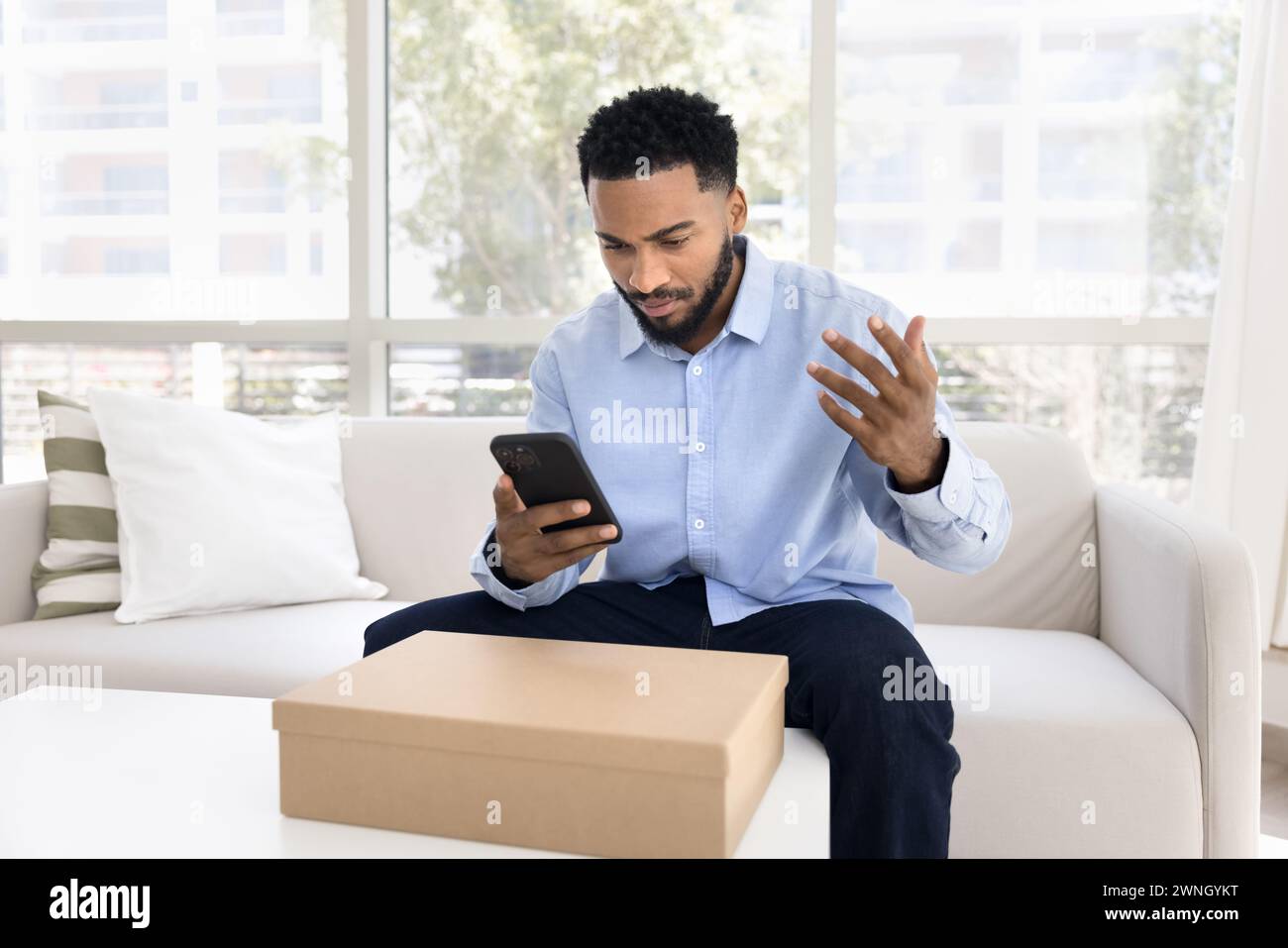 Concerned annoyed young African costumer man using smartphone Stock Photo