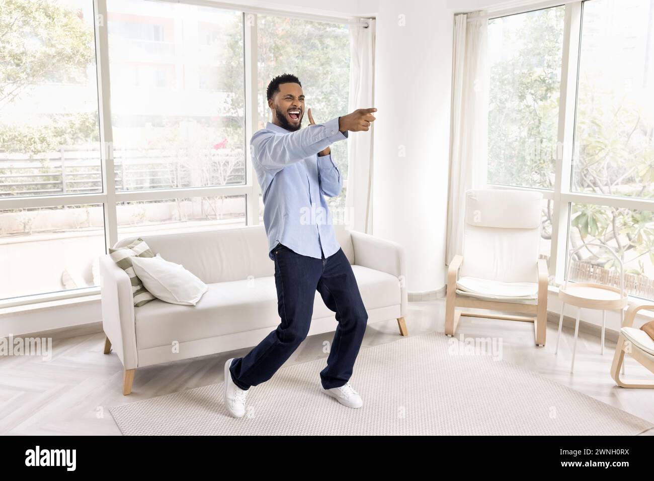 Cheerful overjoyed African man dancing in white colored home interior Stock Photo