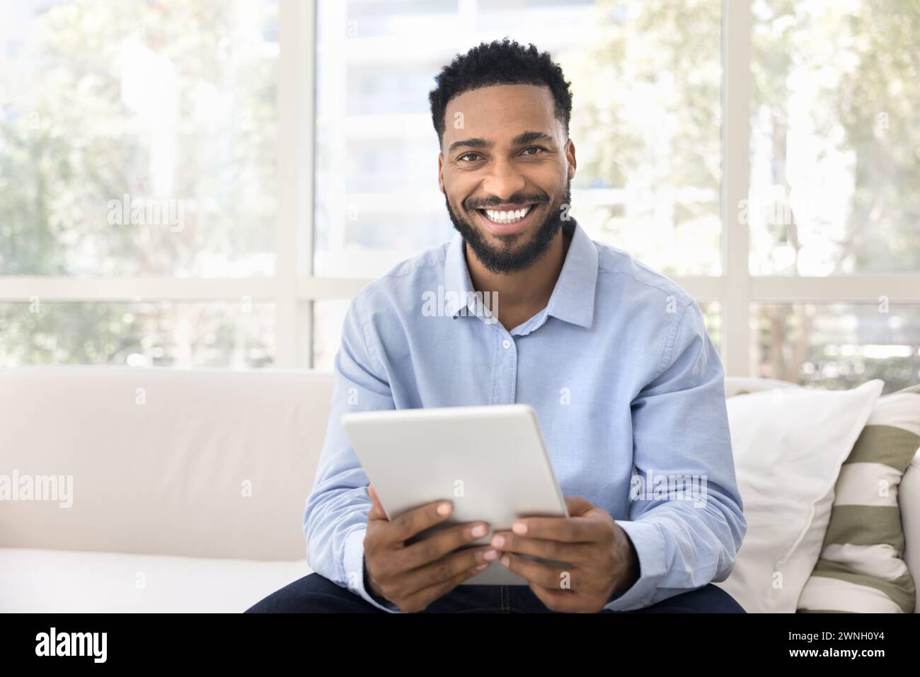 Happy handsome young Black man holding tablet, looking at camera Stock Photo