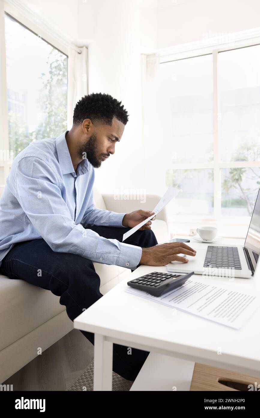 Focuses young African freelancer man working on paper financial reports Stock Photo