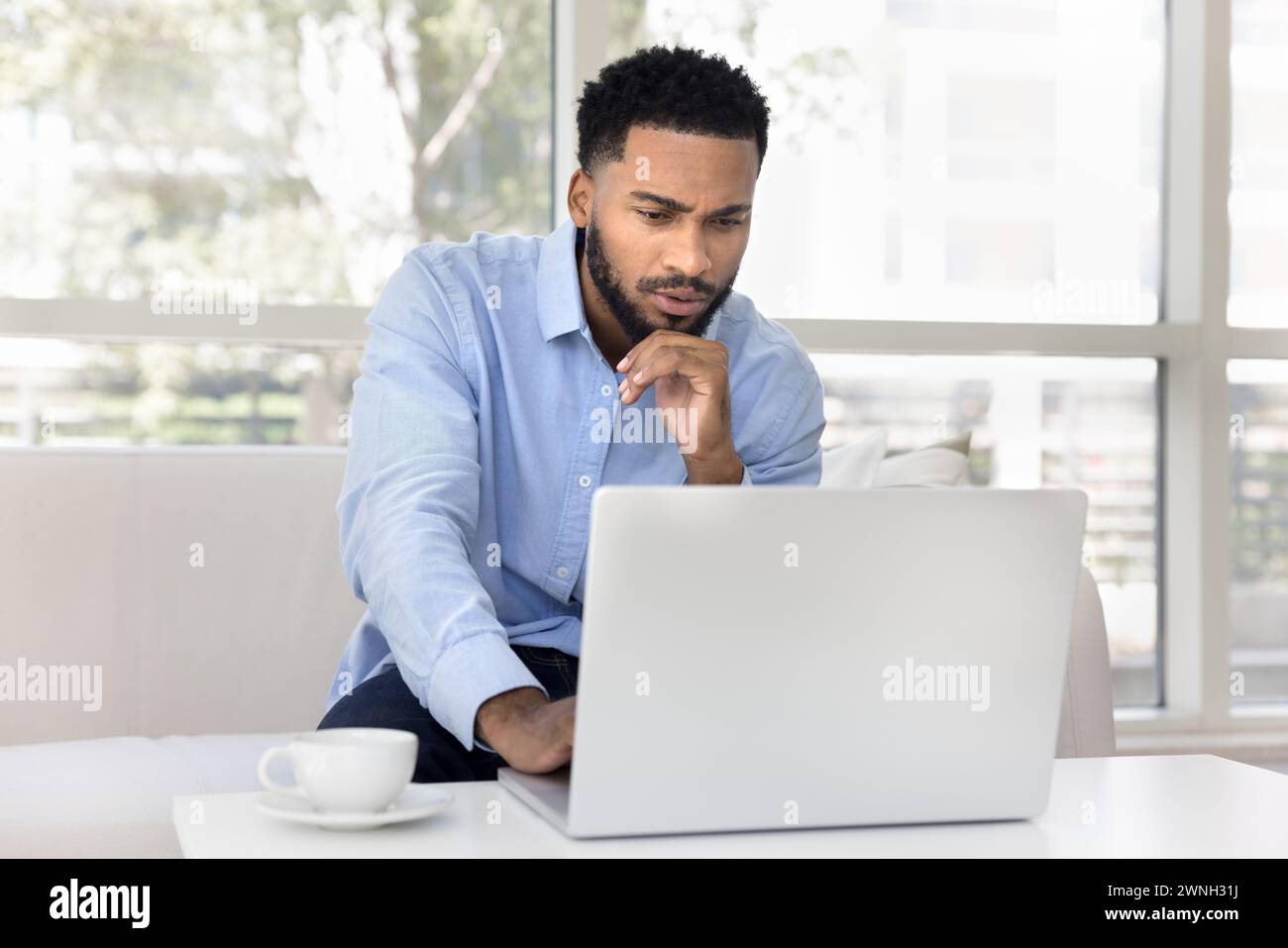 Focused pensive young African freelancer man working at laptop Stock Photo