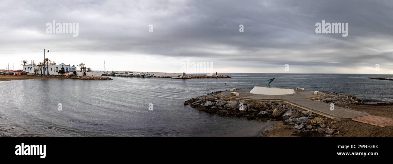 Fotografía panorámica del espigón circular de la playa de El Faro de Marbella y la fuente con La Venus, la dama de Marbella. Cielo tormentoso. Stock Photo