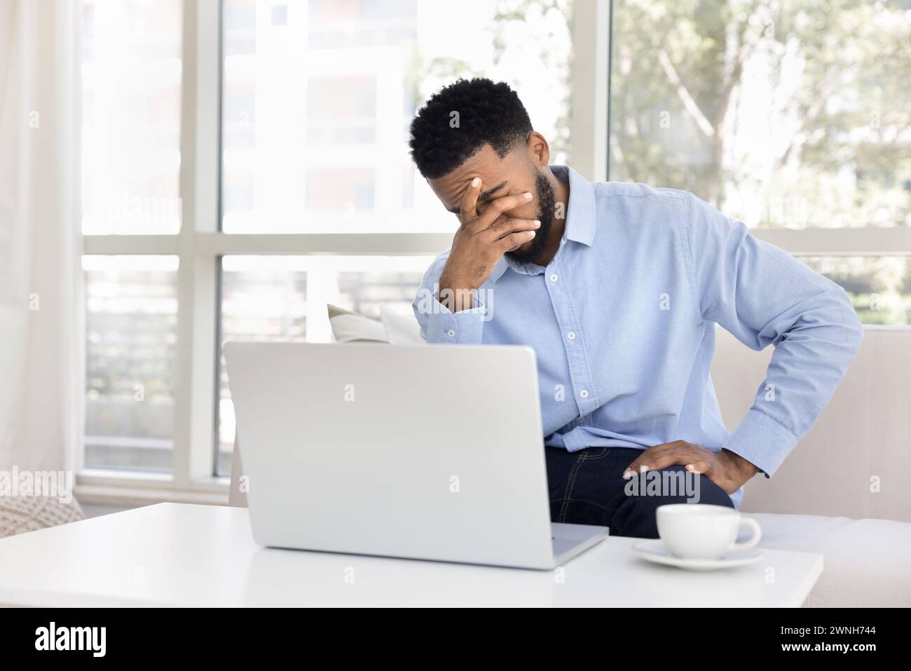 Exhausted frustrated African remote employee man sitting at laptop Stock Photo