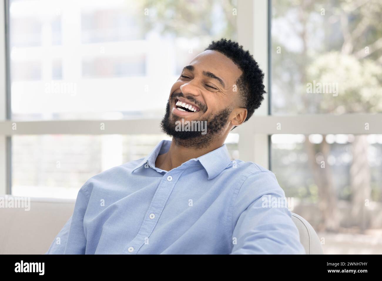 Cheerful handsome young African man sitting on white couch Stock Photo