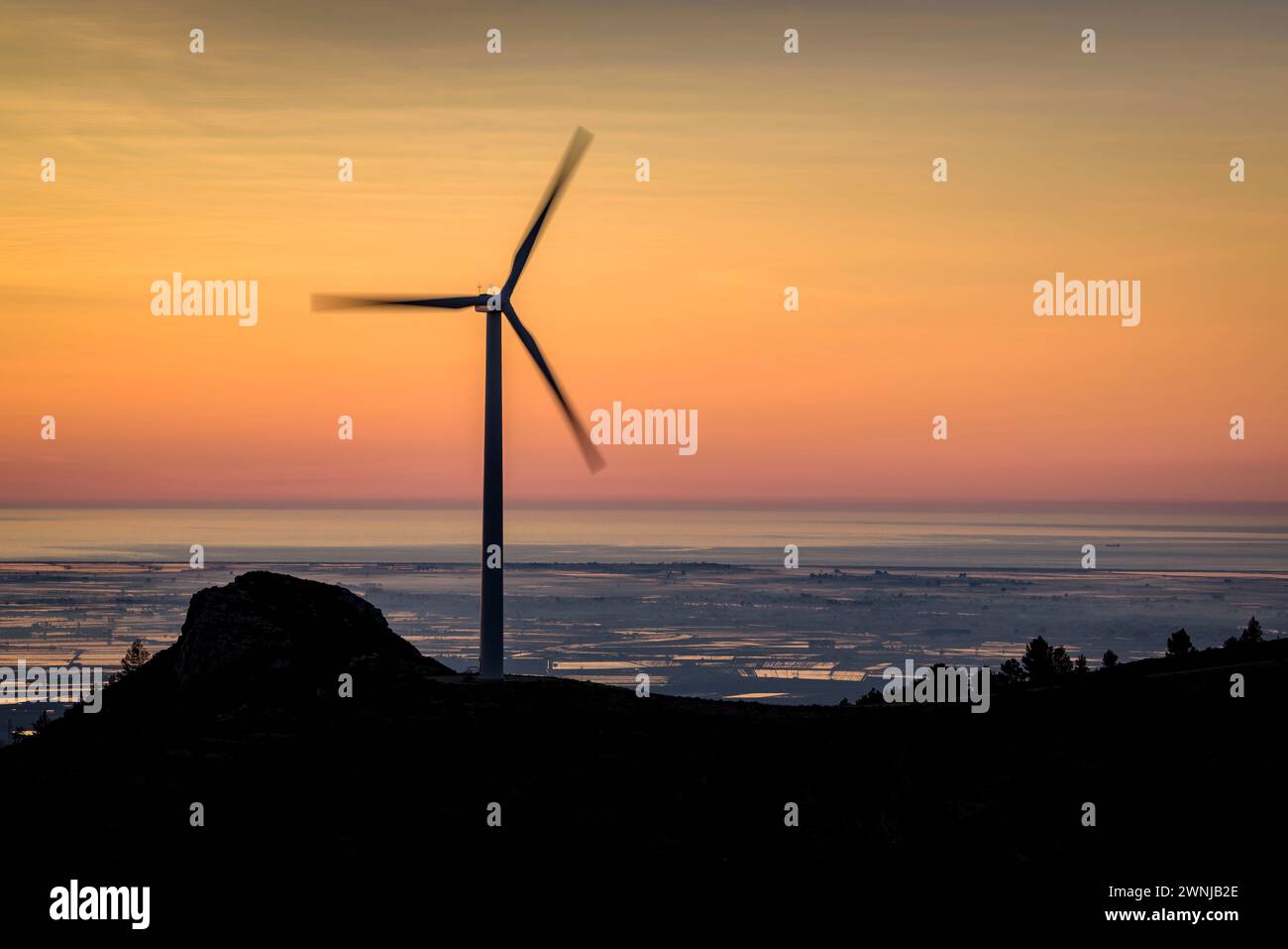 Windmill of the wind farm at sunrise. In the background, the Ebro Delta (Tarragona, Catalonia, Spain) ESP: Molino de viento del parque eólico Stock Photo