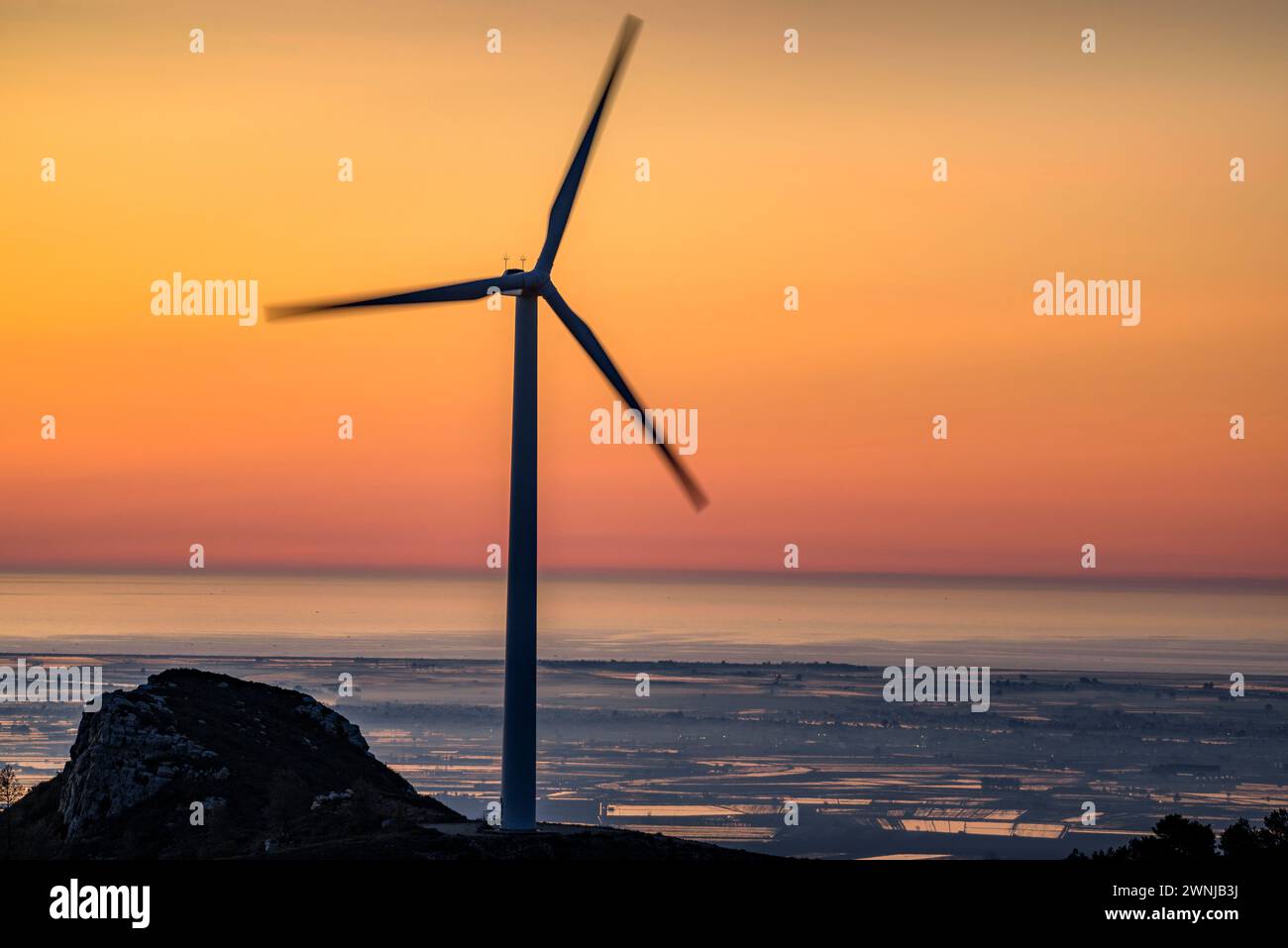 Windmill of the wind farm at sunrise. In the background, the Ebro Delta (Tarragona, Catalonia, Spain) ESP: Molino de viento del parque eólico Stock Photo