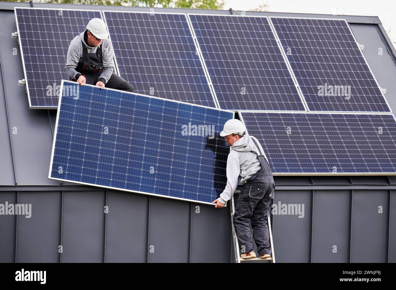 Men electricians installing solar panel system on roof of house ...