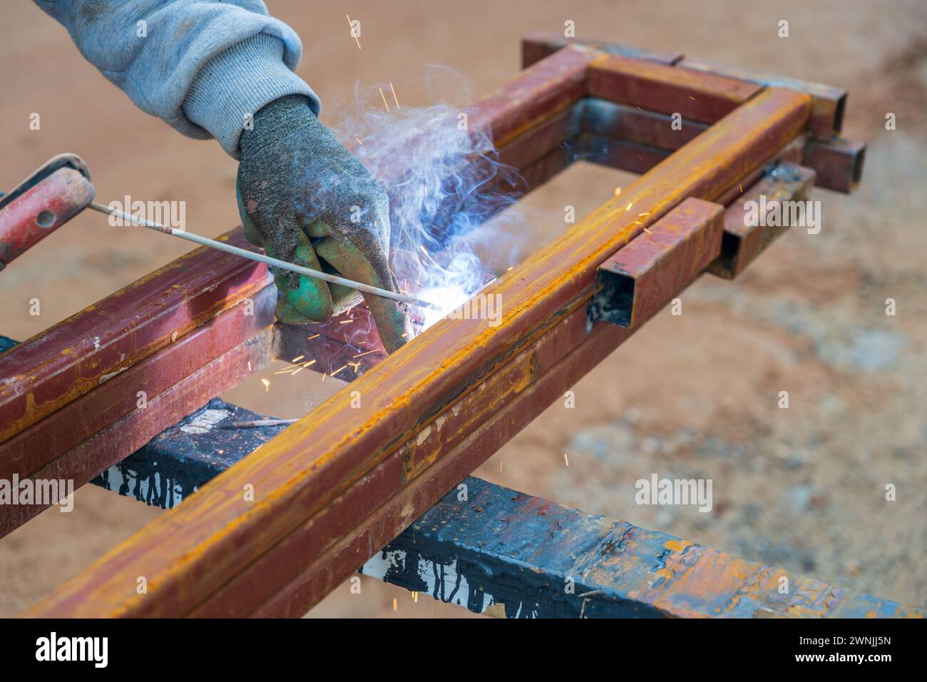 Welder welding two iron profiles at the construction site on a sunny day Stock Photo