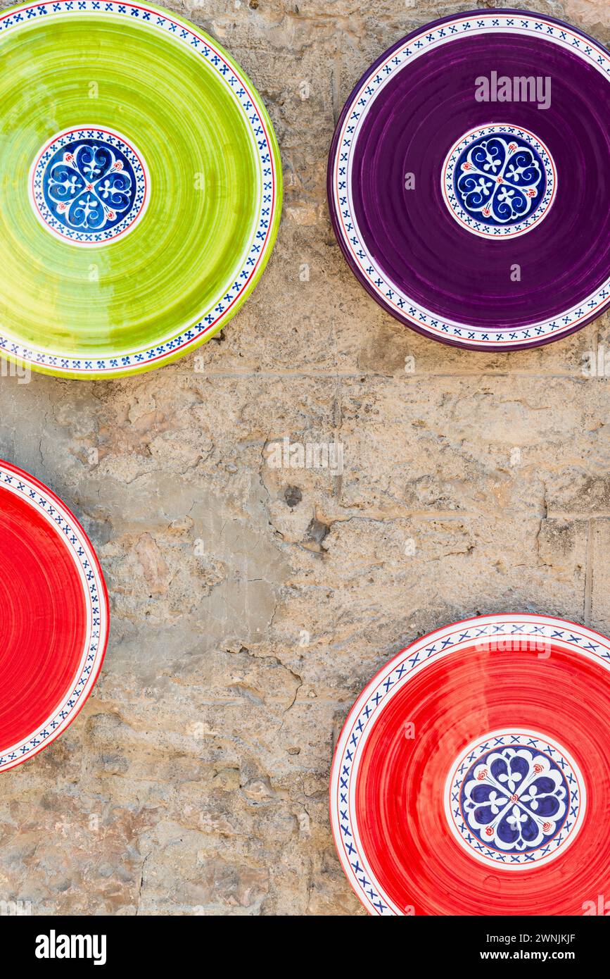 Red, green and purple painted ceramic plates on the stone wall in front