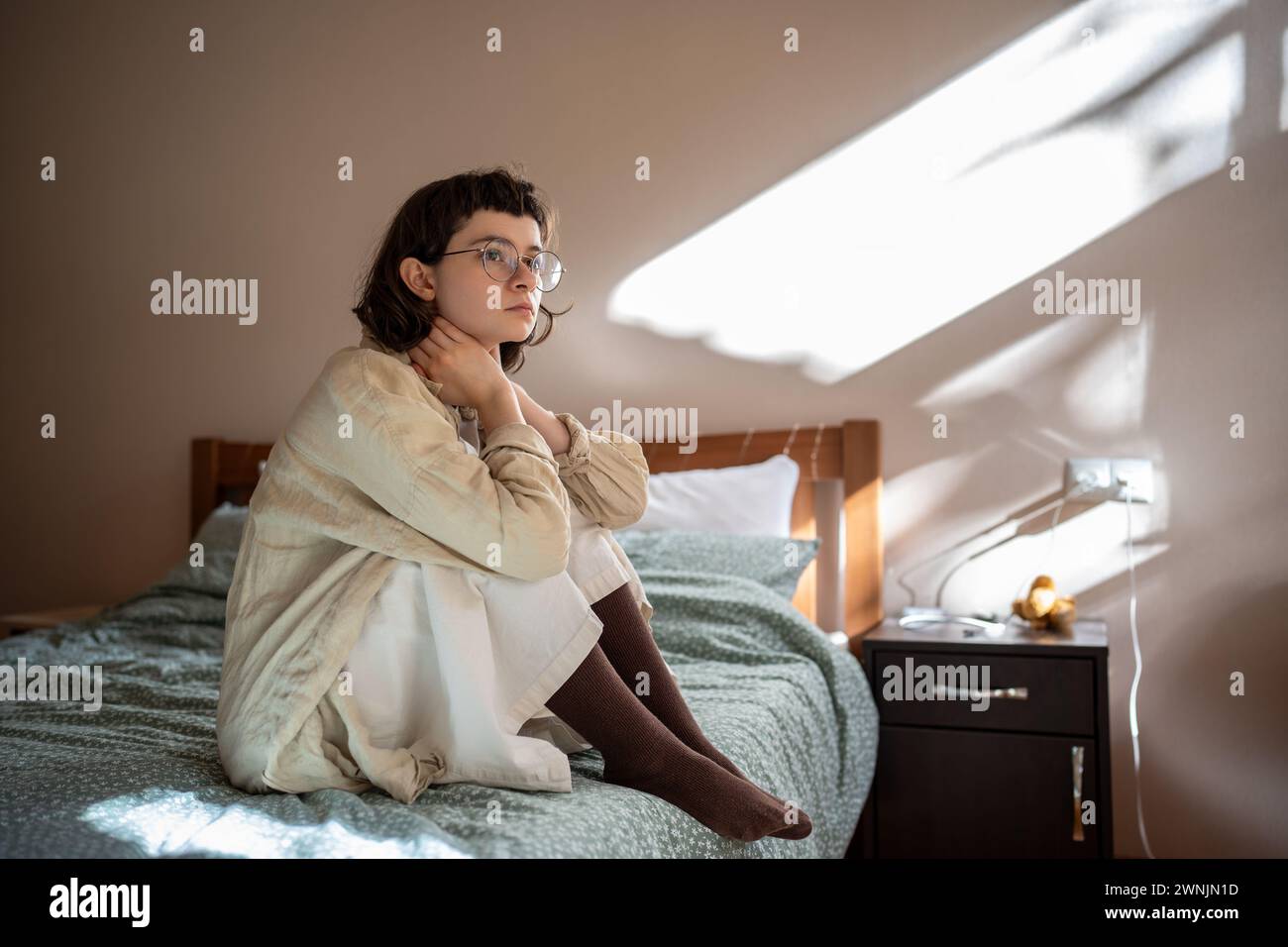 Introverted teenage girl sits on bed in apathetical mood, thinking about troubles, school bullying Stock Photo