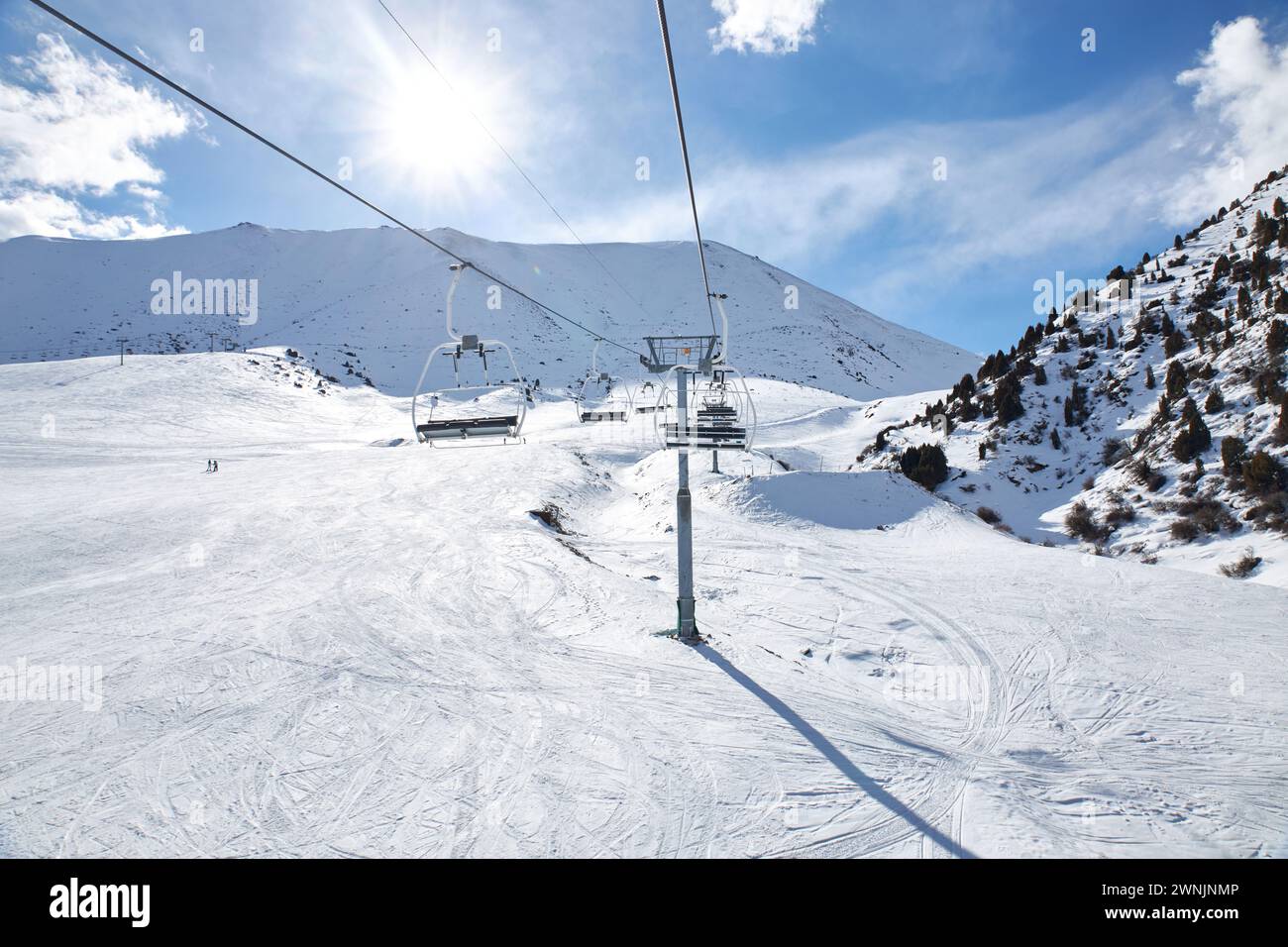 Chunkurchak ski resort in Kyrgyzstan. Empty ski lift seats. Mountain slope at sunny winter day, blue sky. Active recreation skiing and snowboarding. S Stock Photo
