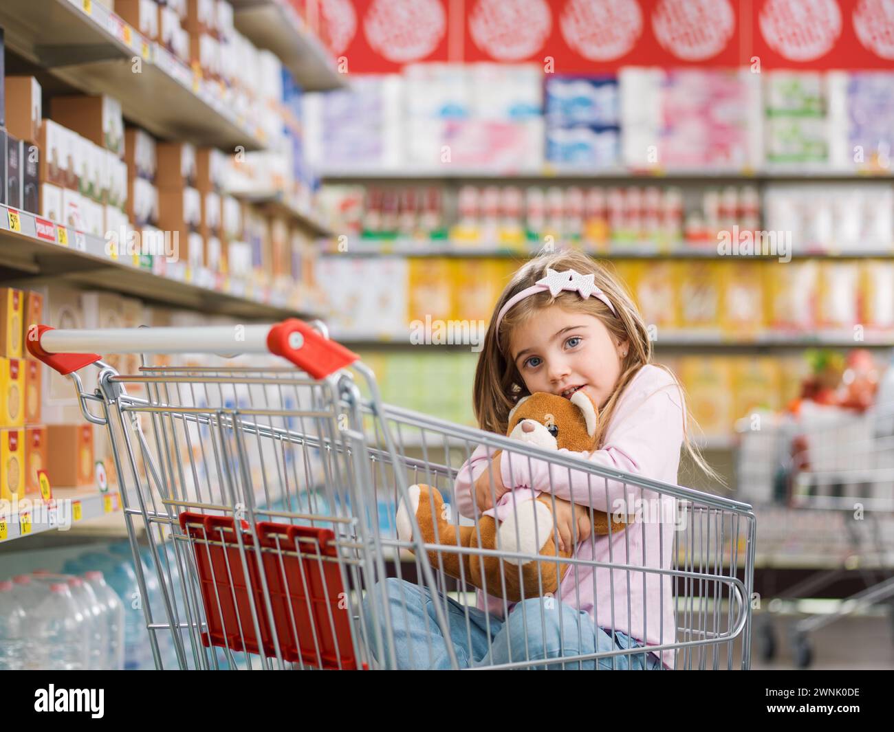 Cute smiling girl at the supermarket, she is sitting in a shopping cart ...