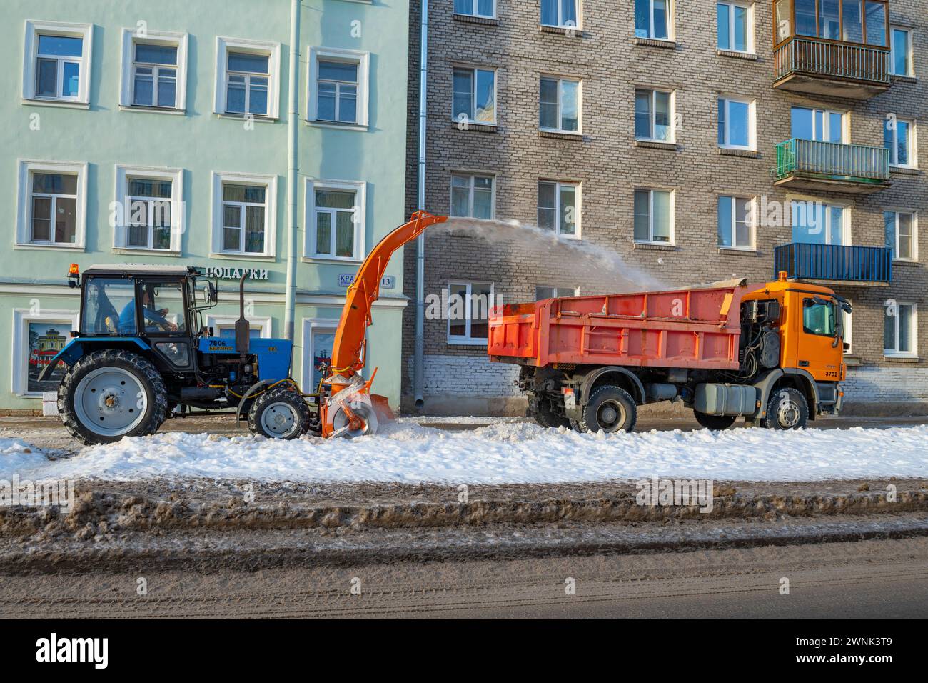 KRONSTADT, RUSSIA - JANUARY 18, 2022:  Tractor MTZ-82.1 tractor with a mounted snow blower clears snow from the sidewalk of a city street Stock Photo