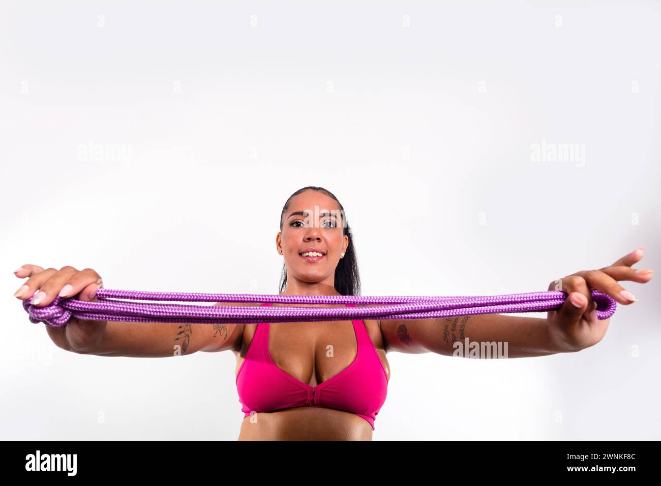 Young gymnast woman holding lilac colored rope for stretching. Against white background. Olympic athlete. Stock Photo