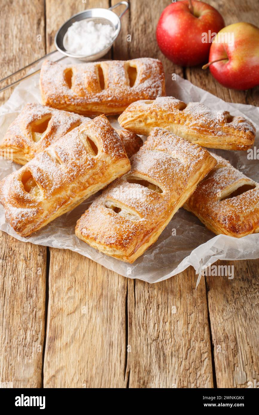 Freshly baked puff pastry with apples on baking paper close-up on a wooden table. Vertical Stock Photo