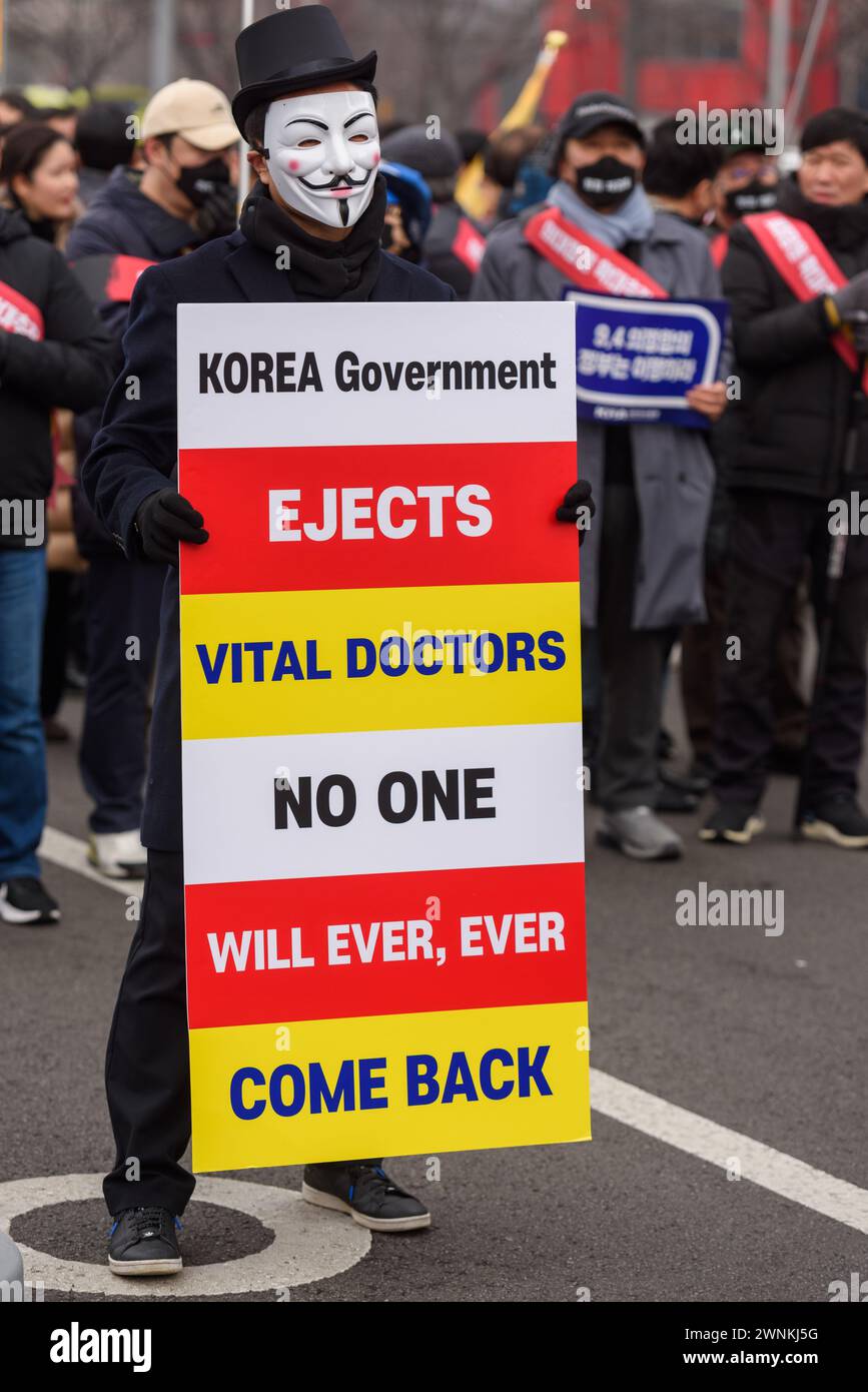 A South Korean doctor wearing a mask holds a placard during a protest. Thousands of senior doctors held a rally in Seoul against the government's medical school quota hike plan as Prime Minister Han Duck-soo hinted at the possible suspension of medical licenses for striking trainee doctors. The rally by members of the Korean Medical Association (KMA), the biggest medical lobby group, came as thousands of trainee doctors have remained off their jobs at general hospitals for the 13th day, protesting the plan to add 2,000 more medical school seats starting next year. Stock Photo