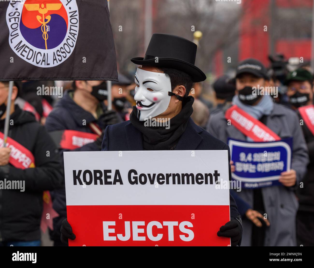 A South Korean doctor wearing a mask holds a placard during a protest. Thousands of senior doctors held a rally in Seoul against the government's medical school quota hike plan as Prime Minister Han Duck-soo hinted at the possible suspension of medical licenses for striking trainee doctors. The rally by members of the Korean Medical Association (KMA), the biggest medical lobby group, came as thousands of trainee doctors have remained off their jobs at general hospitals for the 13th day, protesting the plan to add 2,000 more medical school seats starting next year. Stock Photo