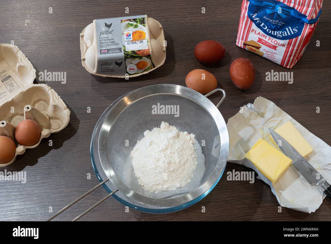 Ingredients for baking a cake on a kitchen worktop - butter, eggs and flour in a sieve for sifting. UK Stock Photo
