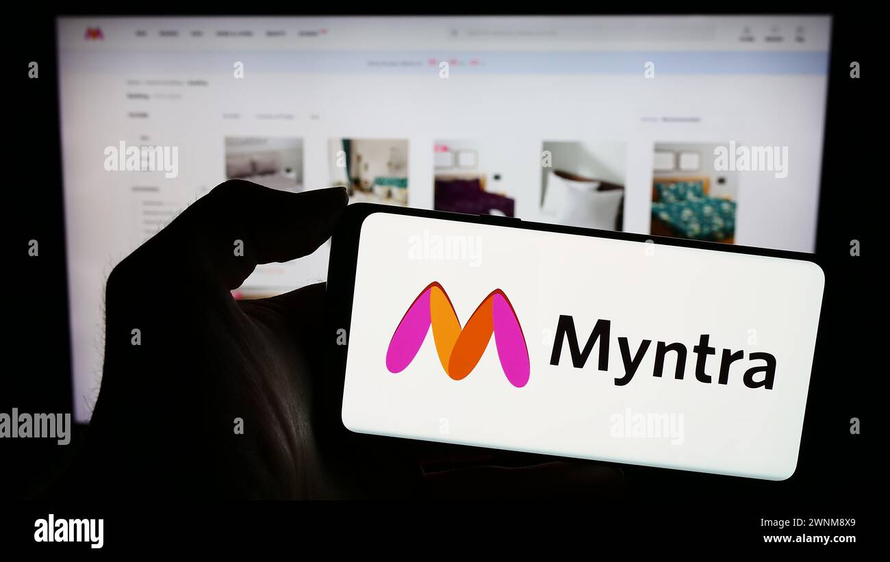 Person holding smartphone with logo of Indian e-commerce company Myntra Designs Pvt. Ltd. in front of website. Focus on phone display. Stock Photo