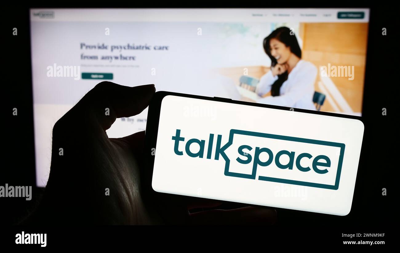 Person holding mobile phone with logo of American online psychotherapy company Talkspace Inc. in front of web page. Focus on phone display. Stock Photo