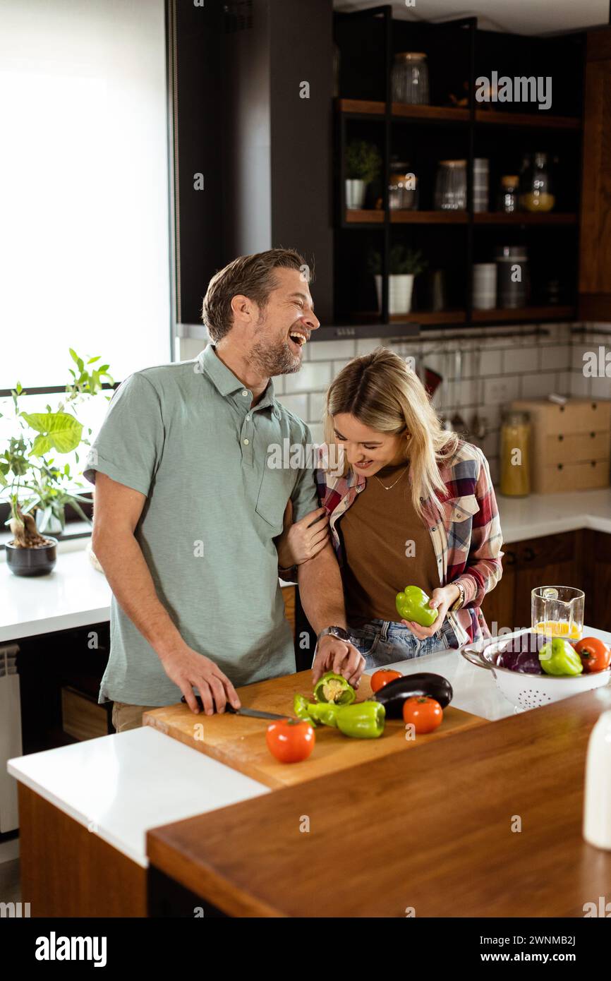 A smiling man and woman chopping fresh vegetables on a kitchen island, enjoying a healthy cooking activity together Stock Photo