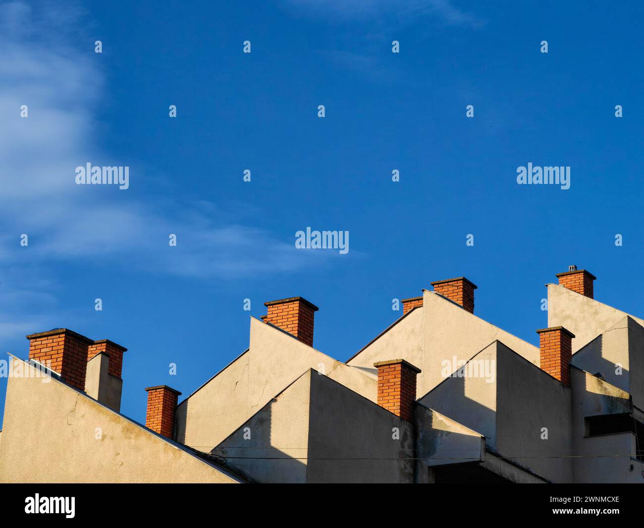 Rising above. Building rooftop brick chimneys against the vast blue skyline. Stock Photo