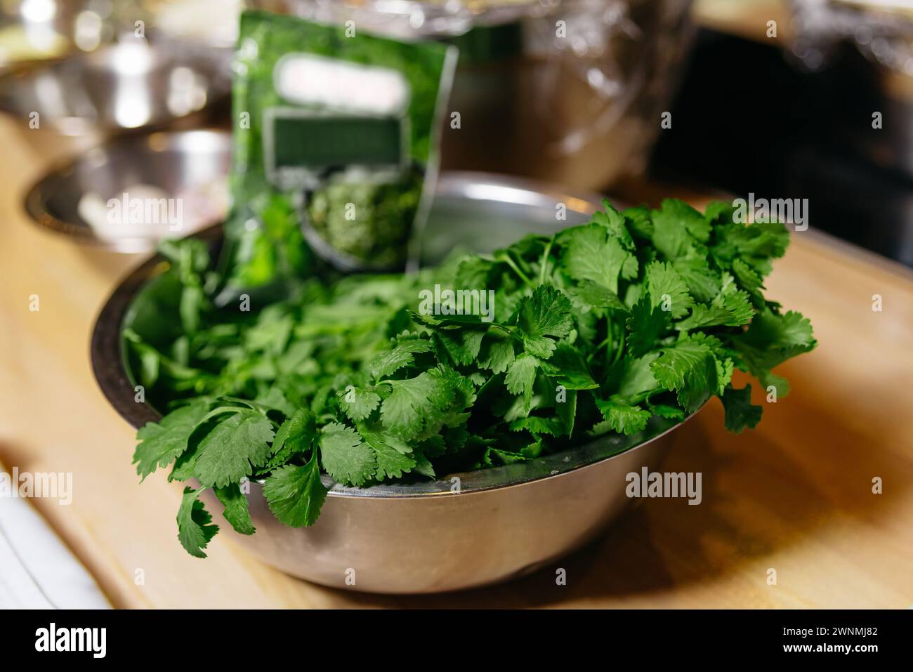 A stainless steel bowl filled with vibrant green cilantro leaves, ready for enhancing flavor in various dishes. Stock Photo