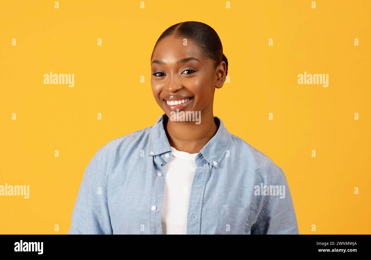 Successful smiling African American woman stands against yellow background Stock Photo