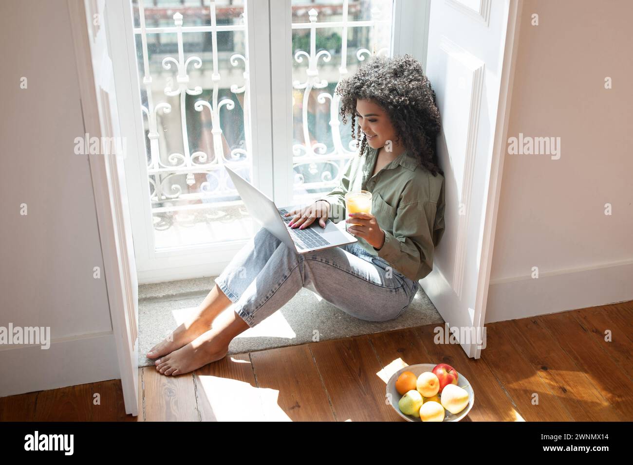 Happy young woman using laptop computer enjoying juice at home Stock Photo