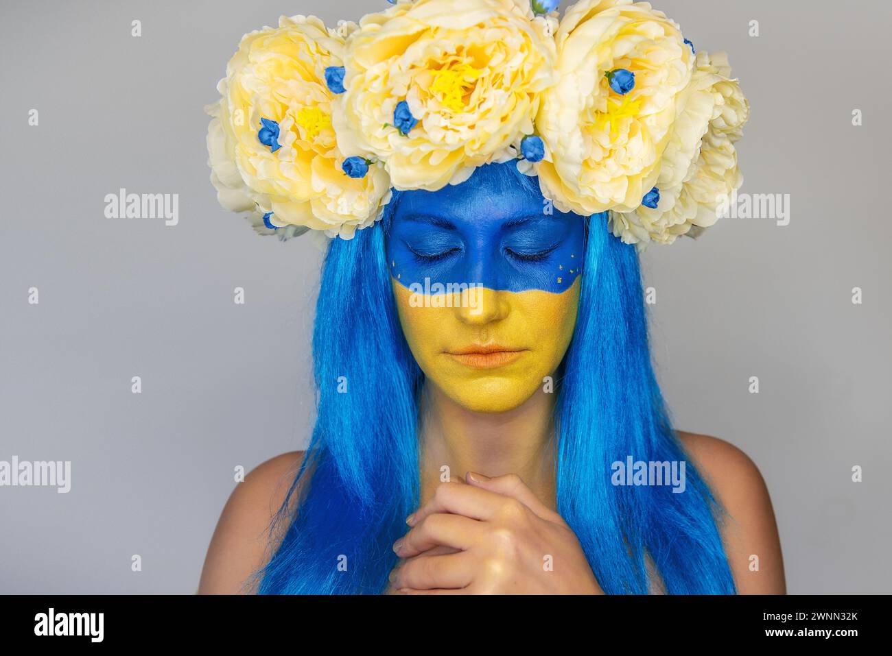 Young woman with yellow blue face art, wreath of peonies on head