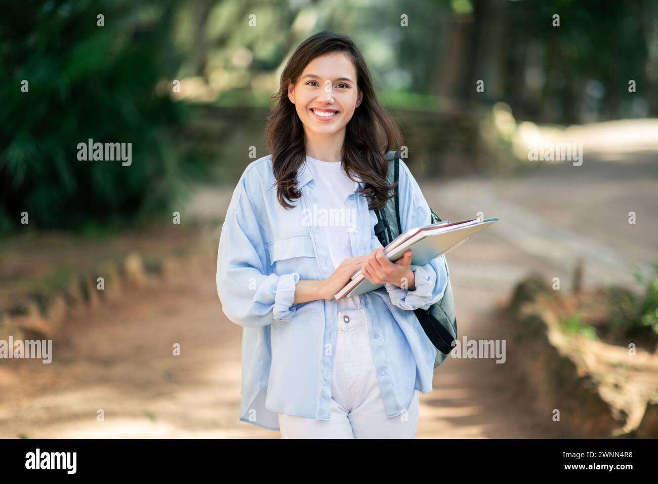 A cheerful young female student with a bright smile walks on a forested ...