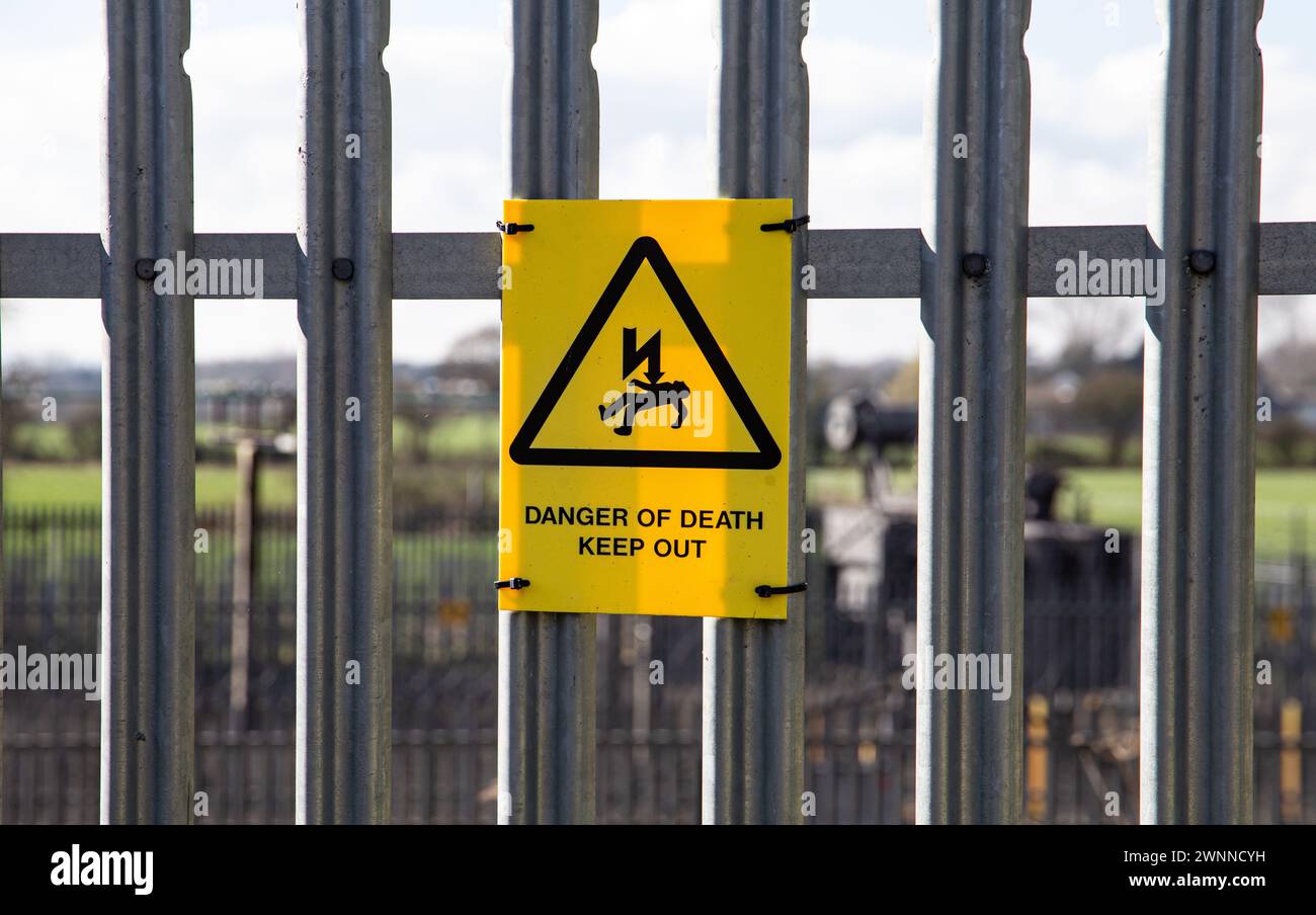 Warning sign of electrocution hazard attached to a metal fence with a rural background Stock Photo