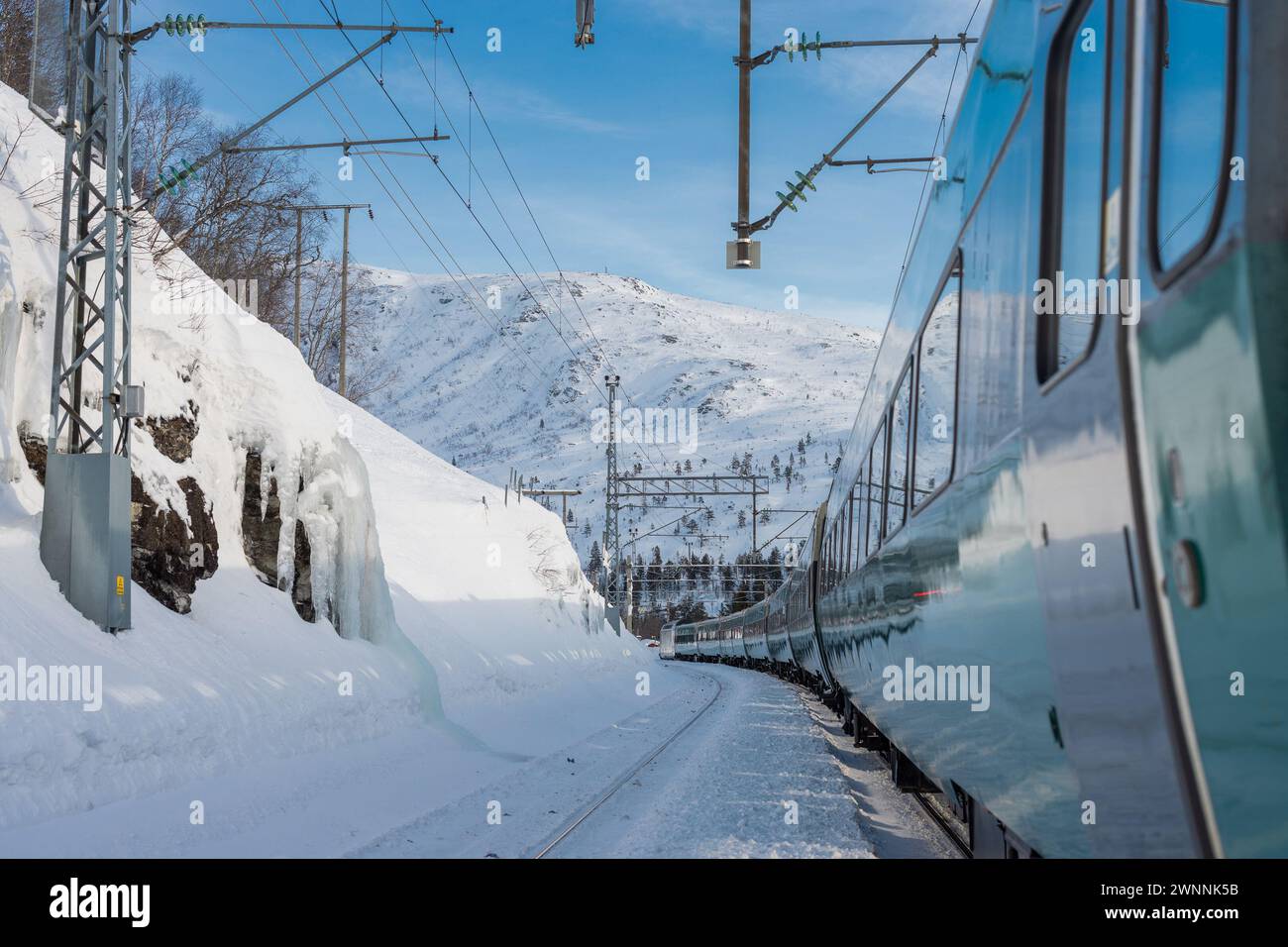 Tran on the famous Bergen - Oslo line is standing on the first track at Mjolfjell train station in the middle of the route. Snow and winter capped mou Stock Photo
