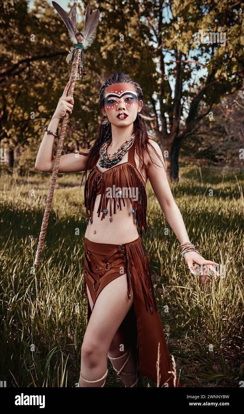 Outdoor portrait of the cute young shamaness (witch doctor) with staff. Beautiful shaman (sorceress) in the forest Stock Photo