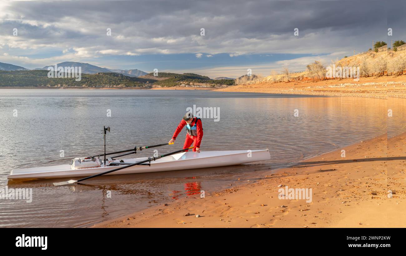 senior rower is rigging his rowing shell on a shore of Carter Lake in northern Colorado in winter scenery Stock Photo