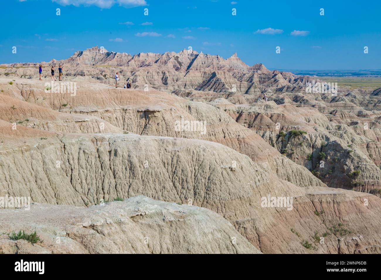 Tourists standing on rock outcropping overlooking colorful layers of ...