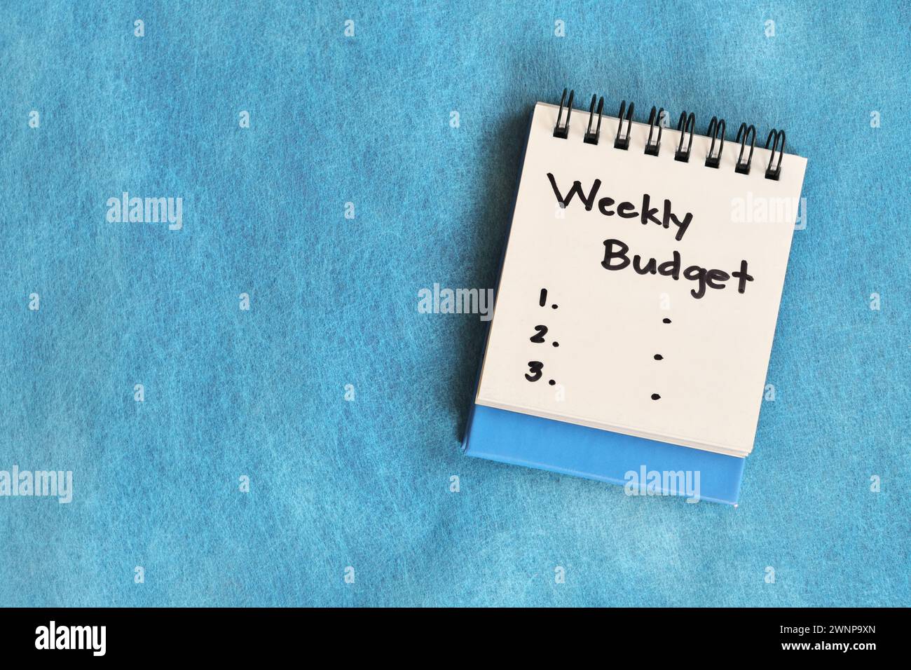 Weekly budgeting concept. White note pad isolated on blue background. Stock Photo
